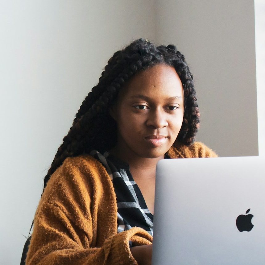 Person with braided hair sitting at a desk using a laptop, accessing online therapy