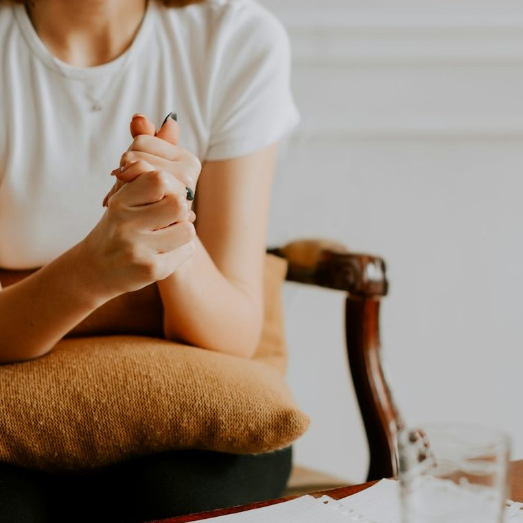 A person sitting with clasped hands, a notepad, and a glass on a table.