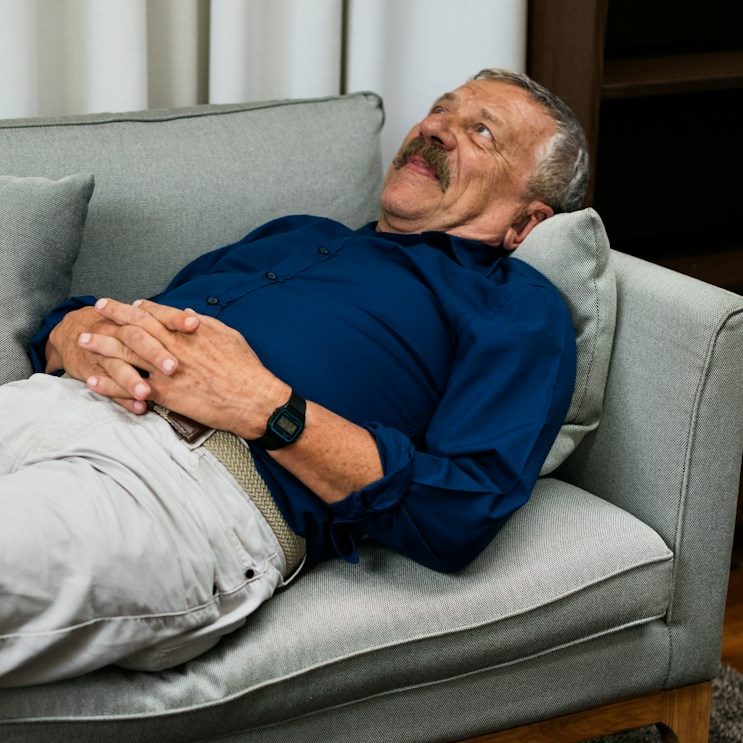A man relaxes on a couch, lying back with a content expression, transformative hypnotherapy